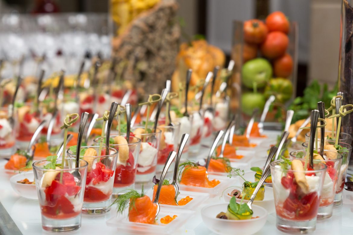 A variety of elegantly presented finger foods in glasses and small plates, featuring ingredients like salmon, mozzarella, cherry tomatoes, and fresh herbs, on a catering table.