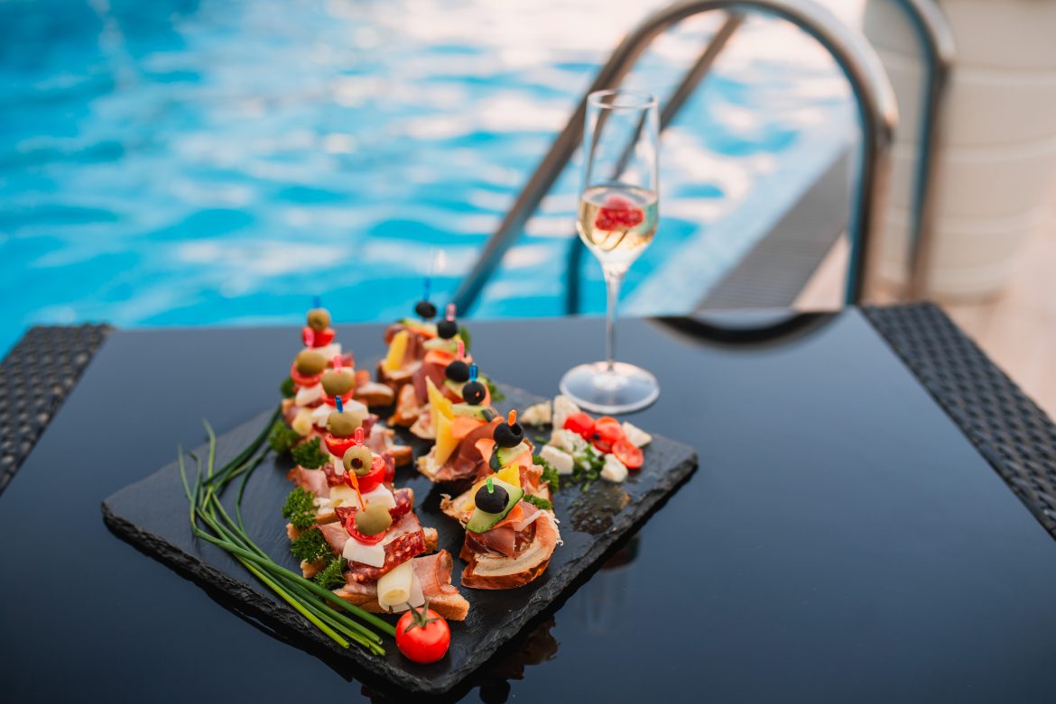 Platter with summer finger foods by the pool, accompanied by a glass of sparkling wine — the perfect setup for pool party catering.