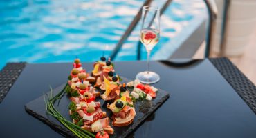 Platter with summer finger foods by the pool, accompanied by a glass of sparkling wine — the perfect setup for pool party catering.