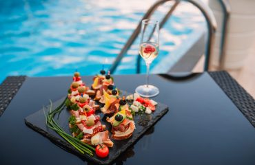 Platter with summer finger foods by the pool, accompanied by a glass of sparkling wine — the perfect setup for pool party catering.