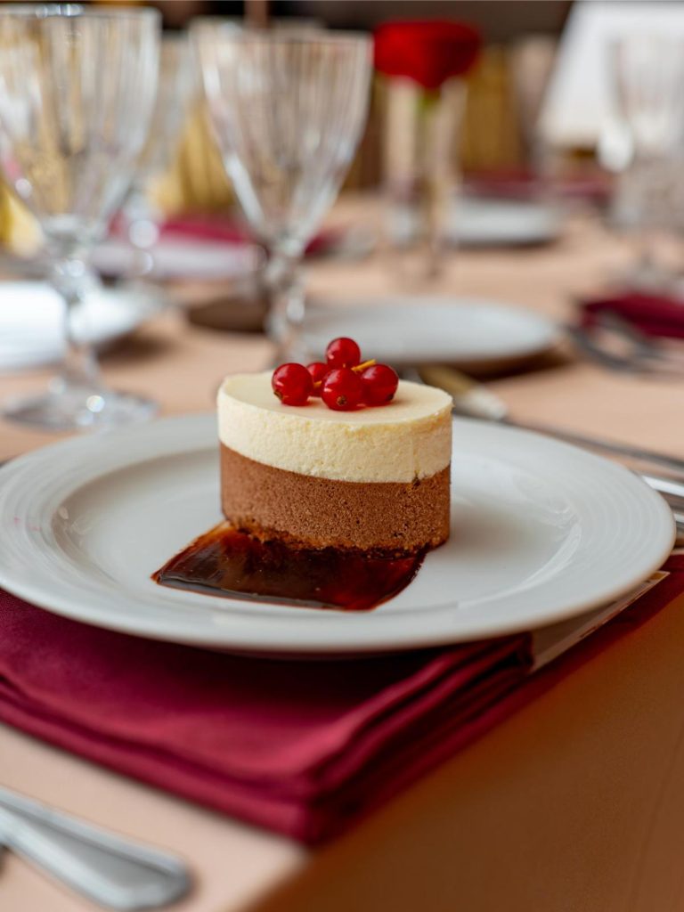 Catering multiple plates arranged on a table, each featuring a sophisticated dessert with ice cream kernel, small dollops of cream, green garnishes, and a rectangular biscuit base, presented on beige, textured ceramic plates.